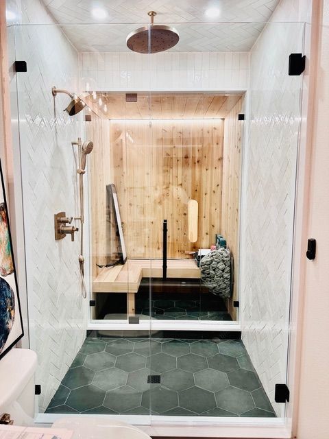 Modern bathroom with glass shower, marble walls, hex tile floor, and wooden bench seating area