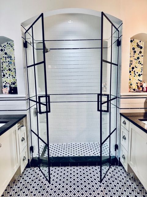 Black metal shower enclosure with open doors in a white kitchen, showing a tiled interior and floor.