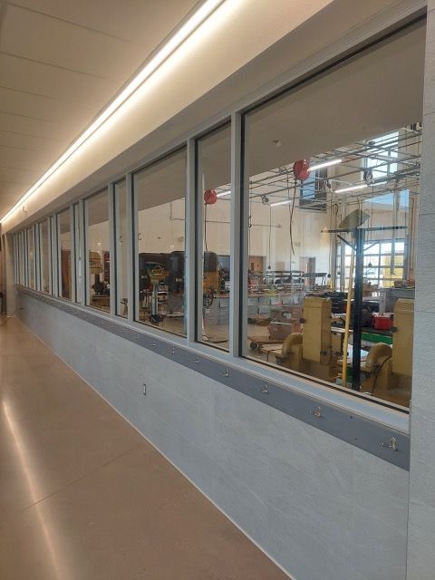 Long hallway beside a large window into a workshop or classroom with desks and equipment inside