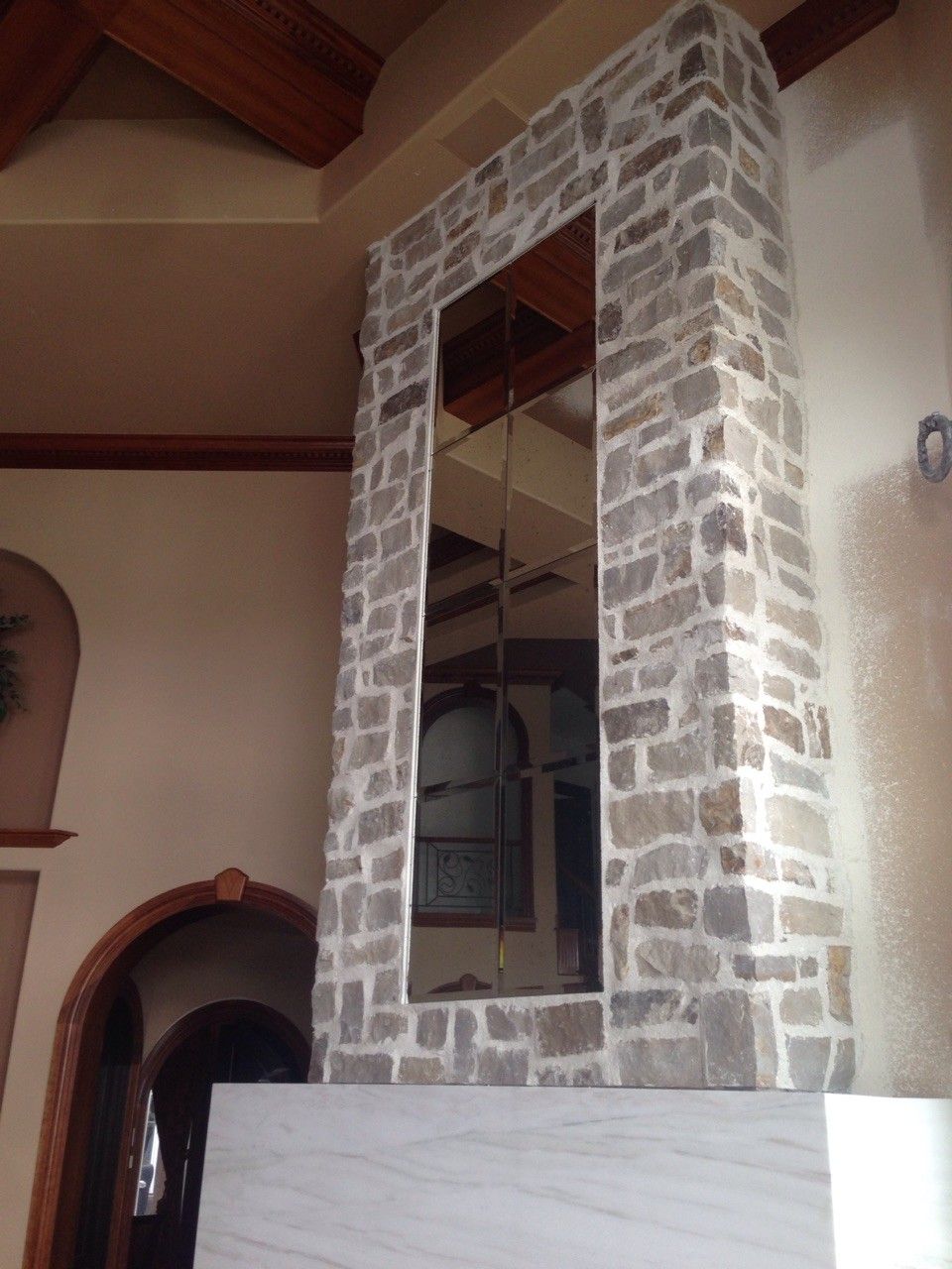 Stone fireplace wall with a tall mirror in a room with wooden ceiling beams