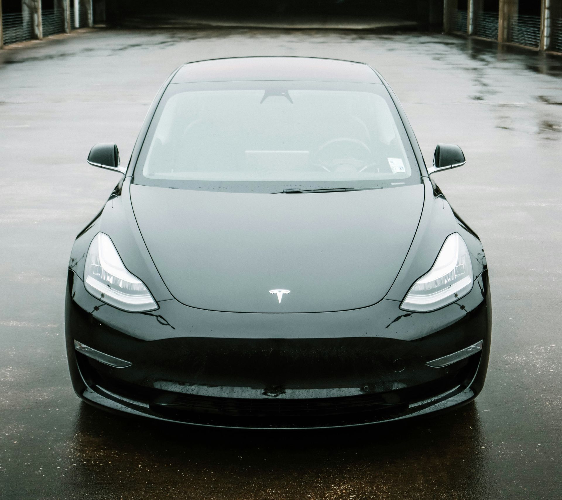 Black Tesla Model 3 sedan parked outdoors on wet pavement.