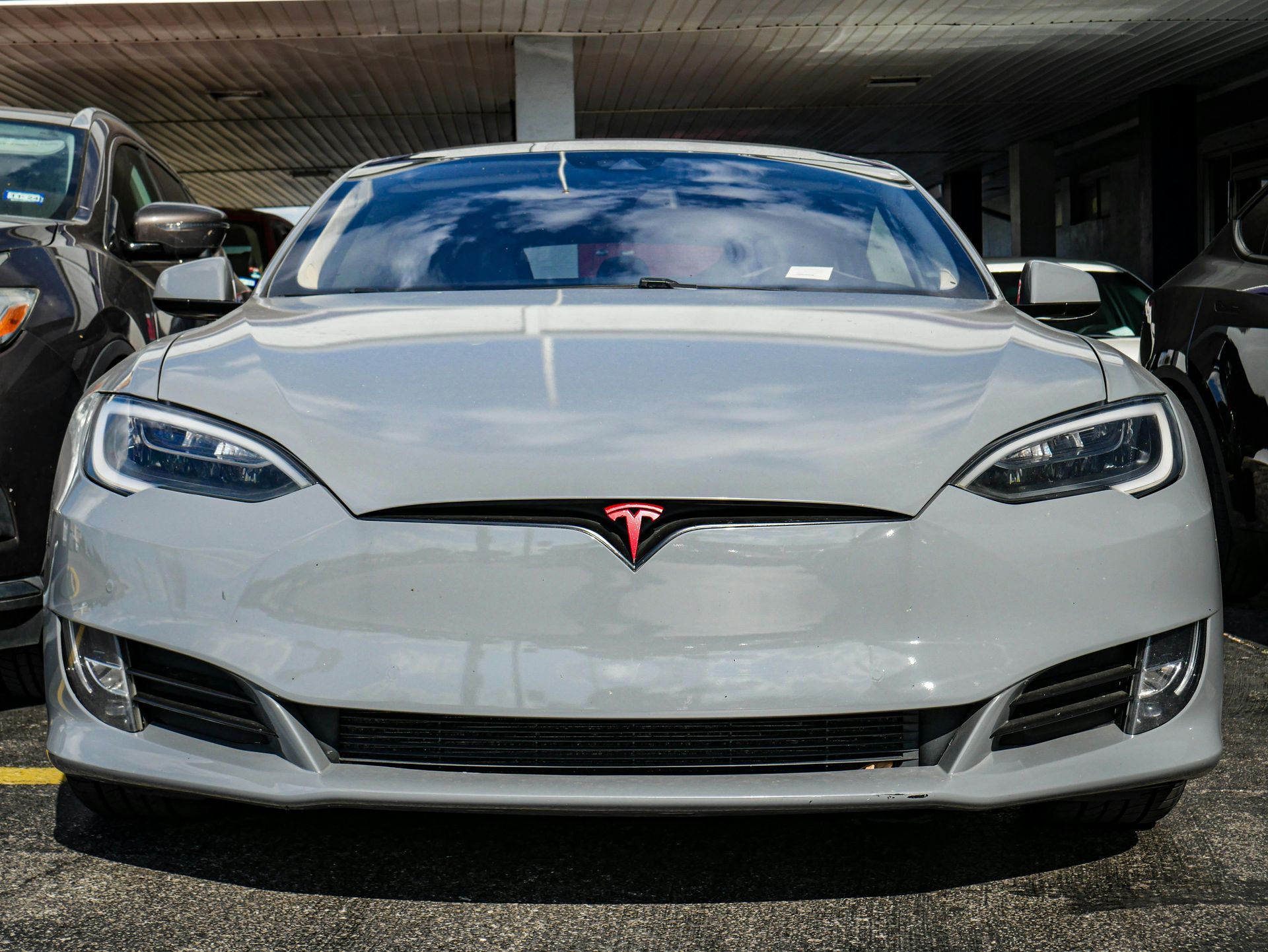 Gray Tesla Model S electric car parked outdoors. Red Tesla emblem is visible.