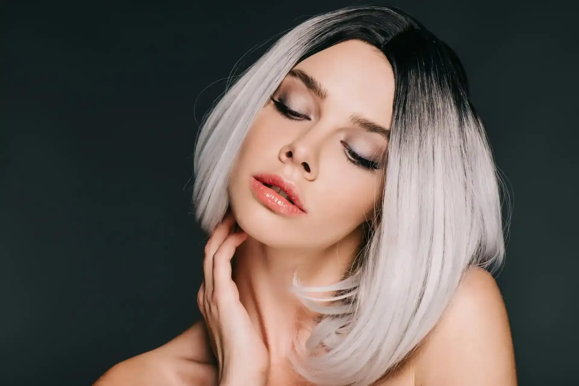 Donna con acconciatura a caschetto, occhi chiusi e mano sul collo; capelli sfumati dal nero all'argento.