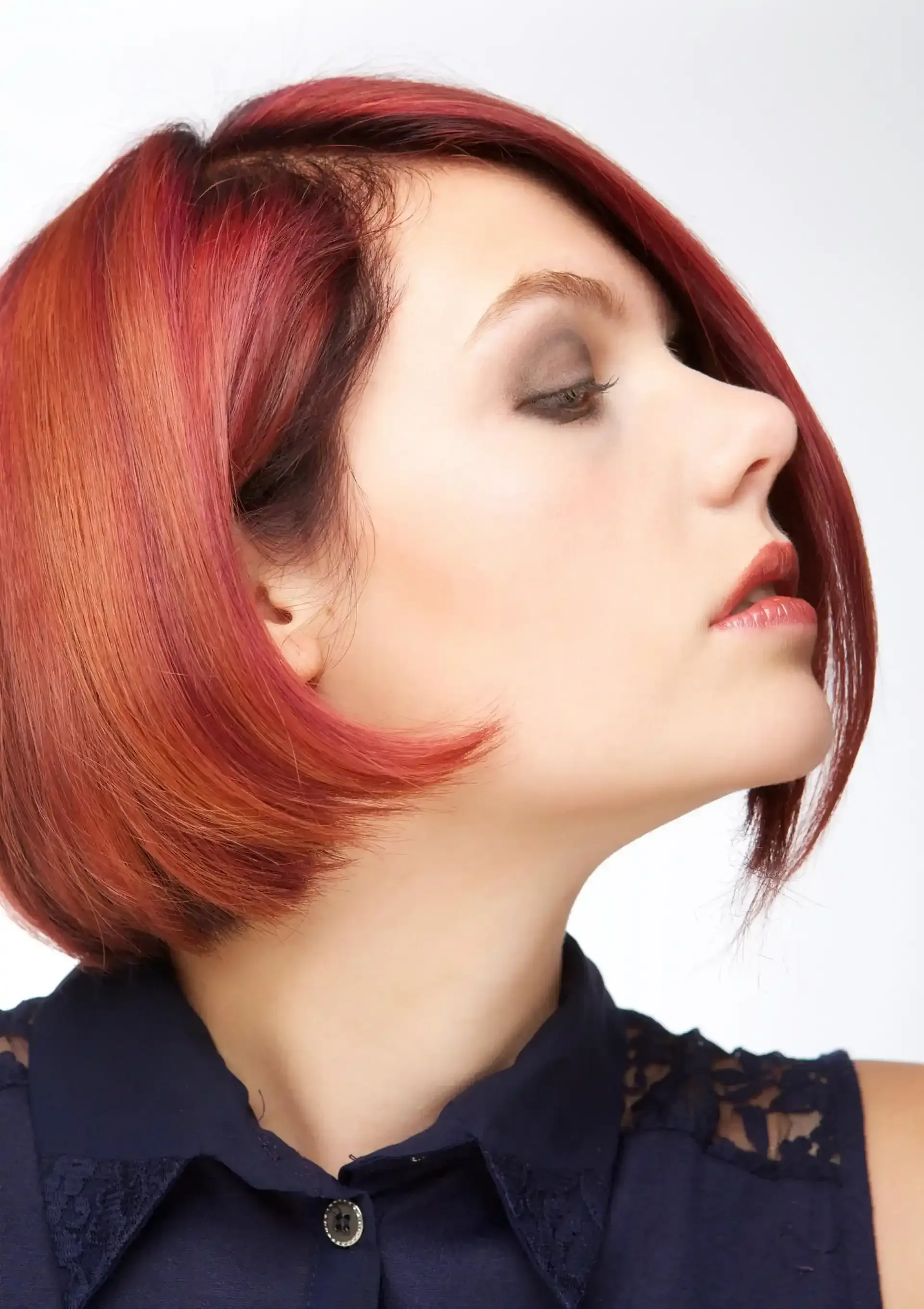 Donna con caschetto rosso obliquo, sguardo rivolto a destra. Indossa una camicia blu navy con colletto.
