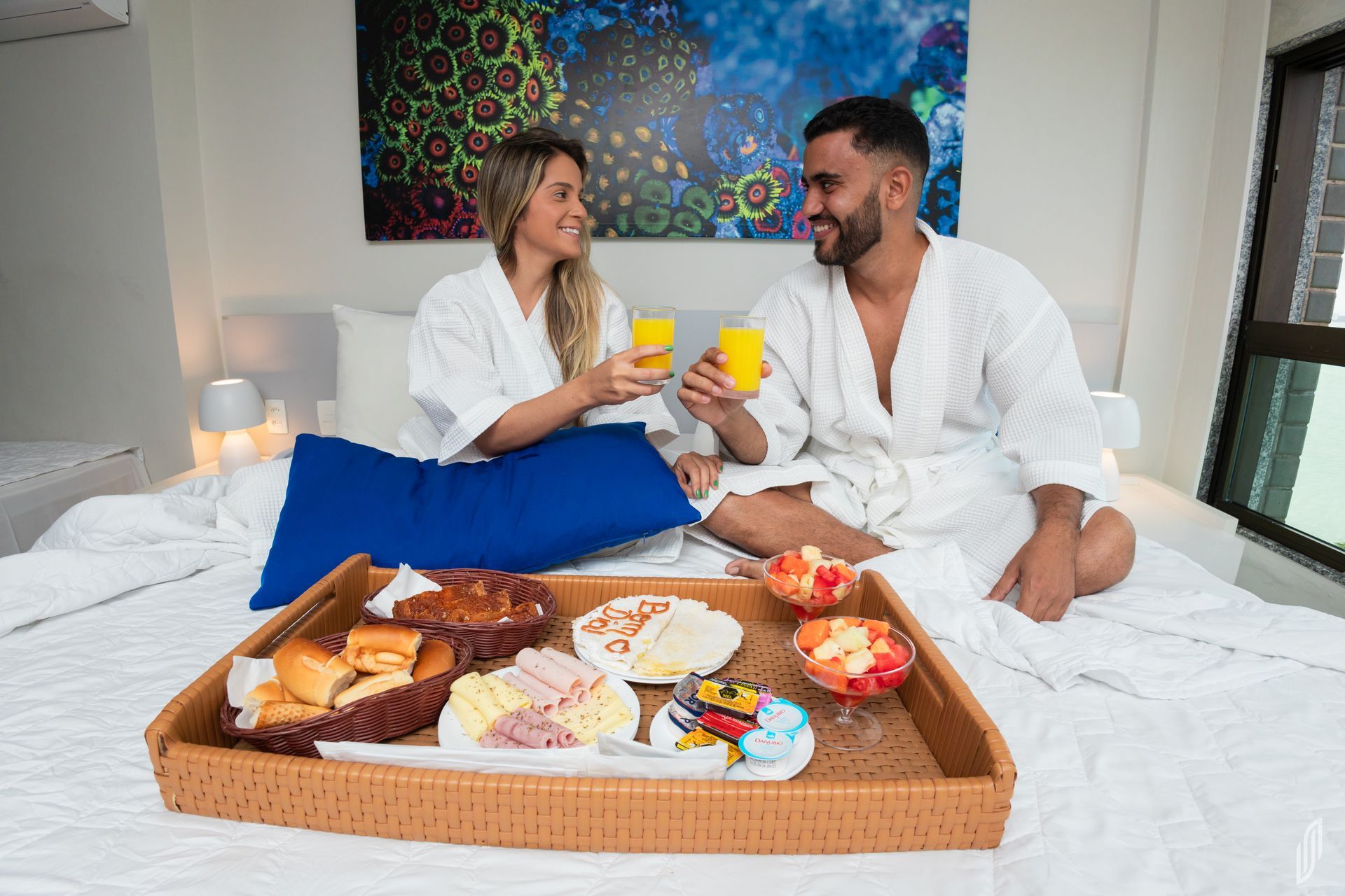 Casal curtindo o café da manhã na cama, brindando com suco de laranja celebrando o momento.