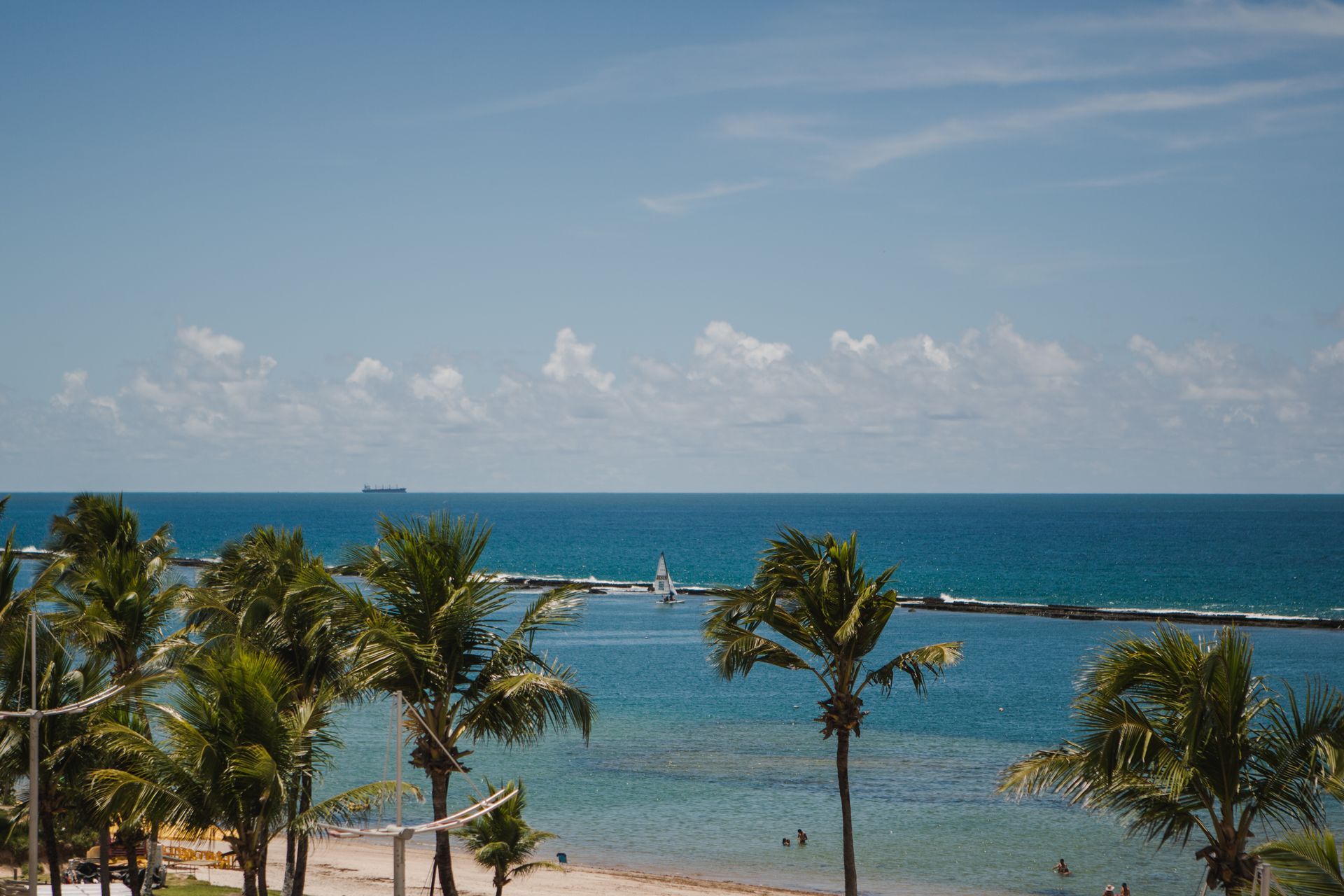 Vista aérea da Praia do Francês, mostrado os múltiplos tons de azul do mar e os coqueiros.