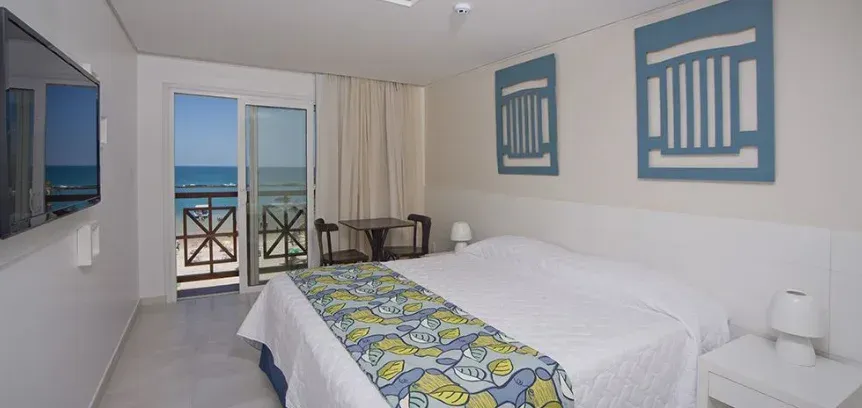 Um quarto de hotel com uma cama grande e uma varanda com vista para o oceano.