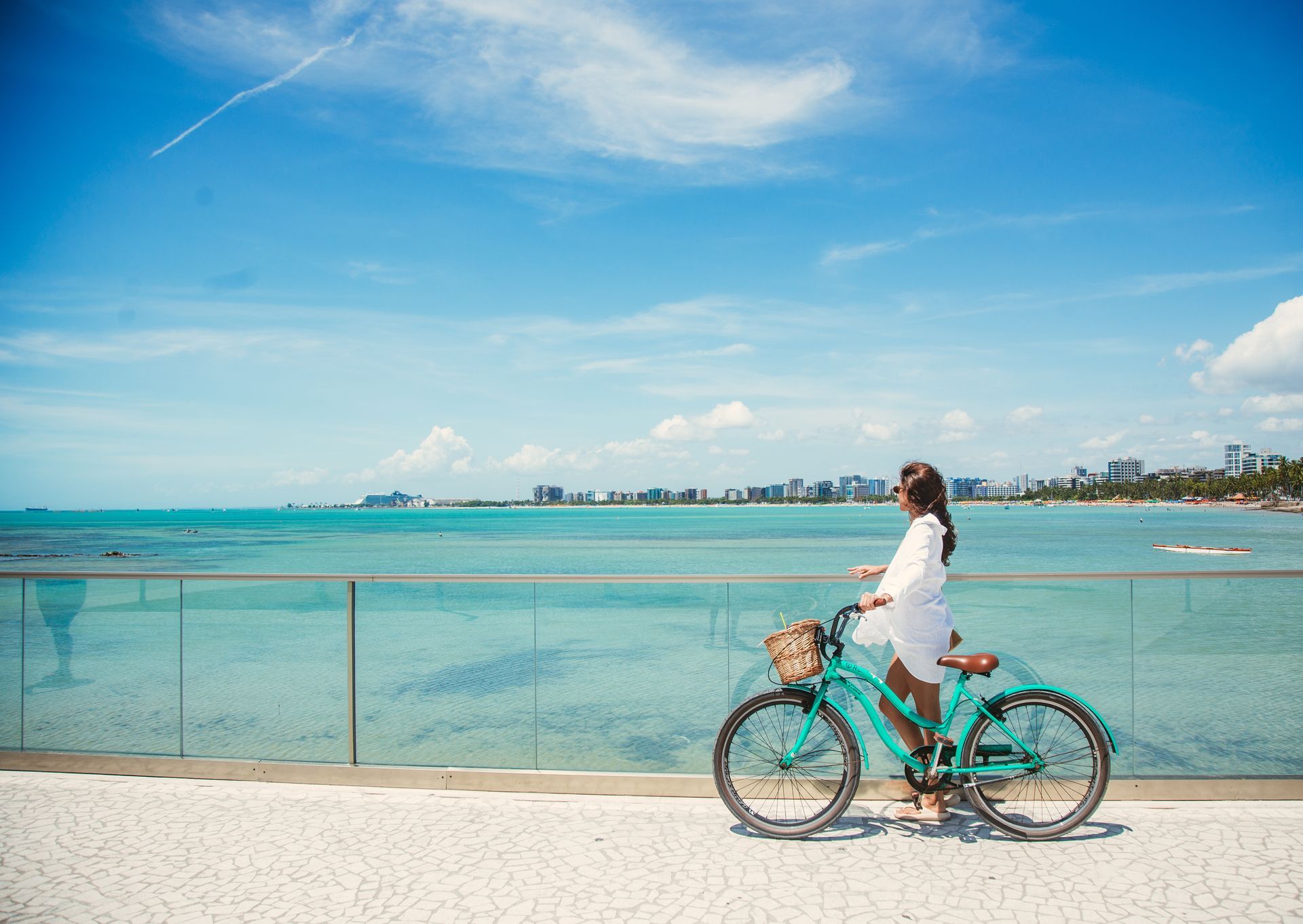 Mulher com biciclea verde, em um dia de sol no Marco dos Corais, ponto turístico da Ponta Verde.