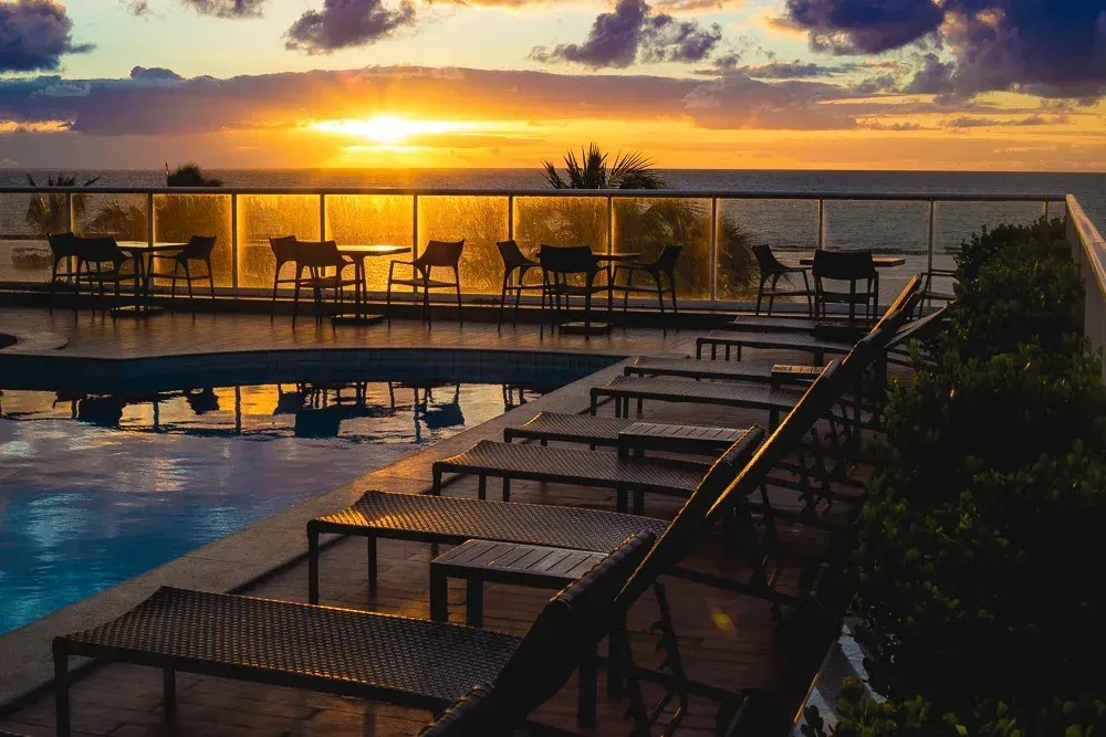 Um pôr do sol sobre uma piscina com espreguiçadeiras e mesas.