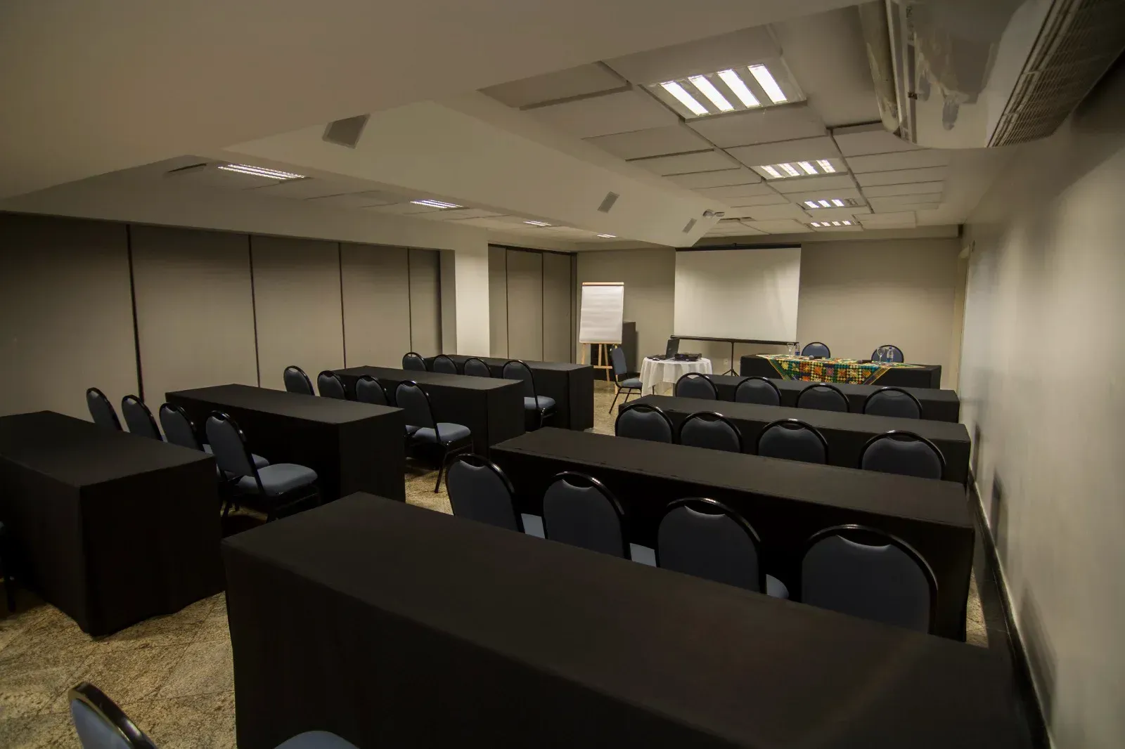 Uma sala de conferências com mesas e cadeiras e uma tela de projetor.