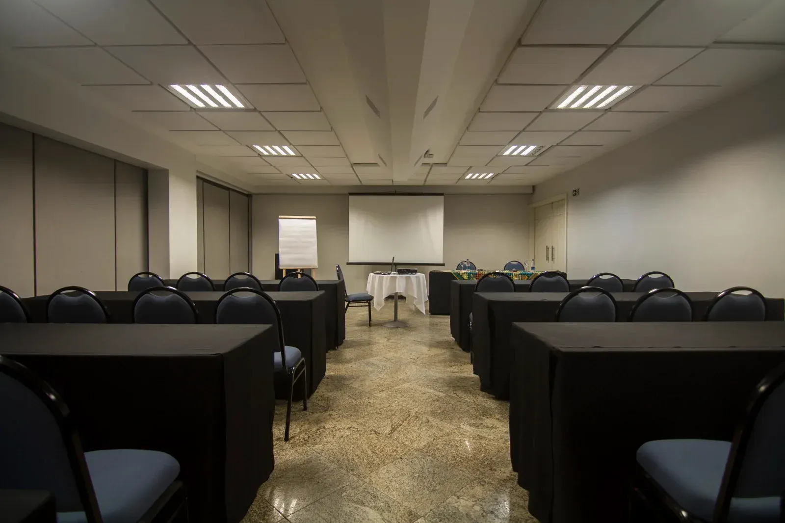 Uma sala de conferências com mesas e cadeiras e uma tela de projetor.