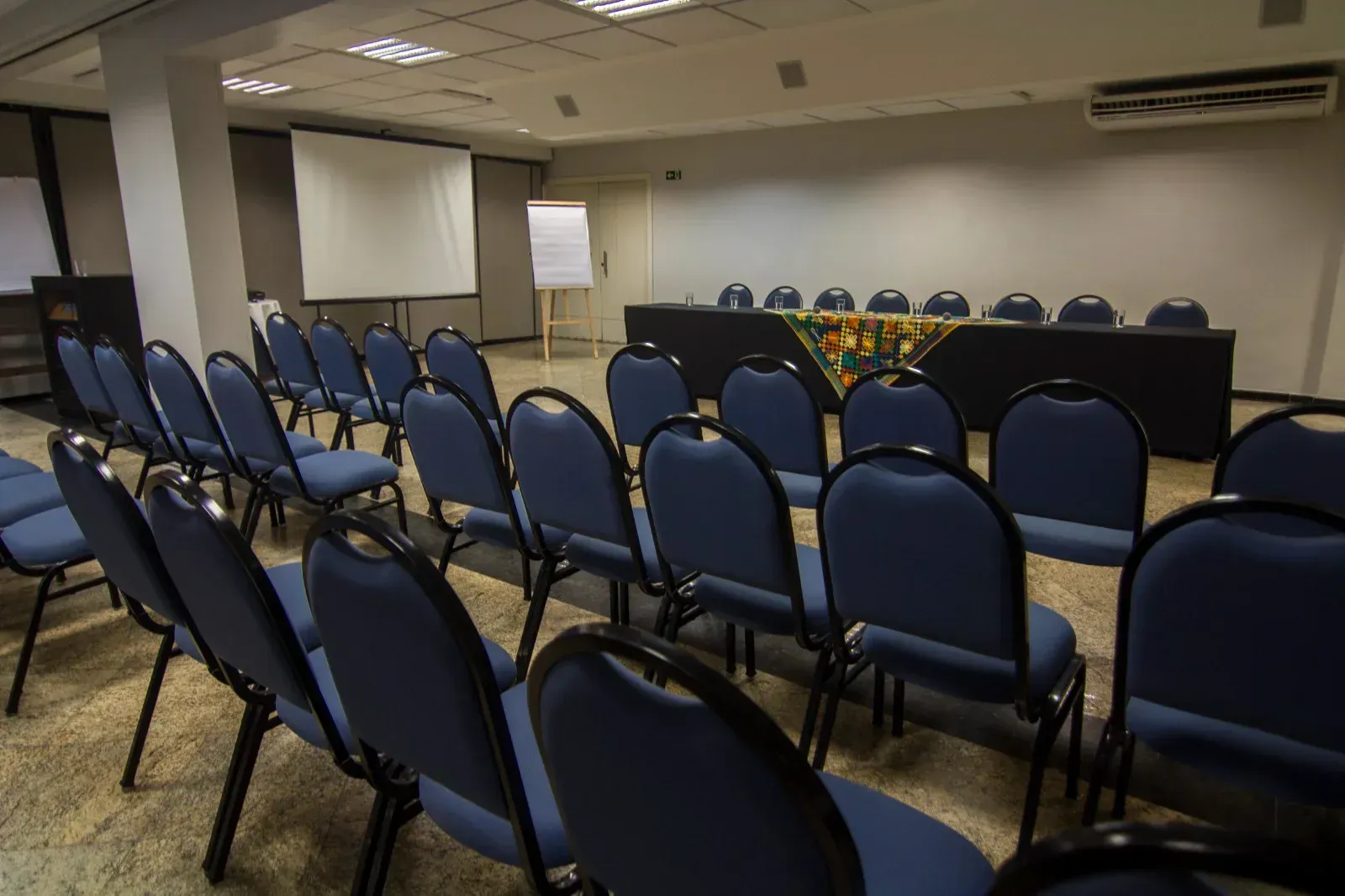 Uma sala de conferências com cadeiras azuis e uma tela de projetor