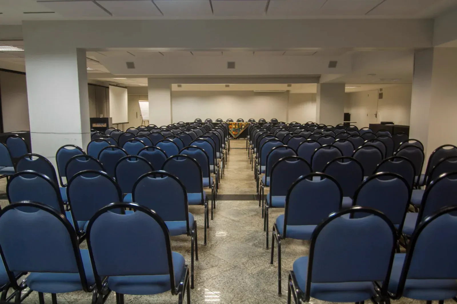 Fileiras de cadeiras azuis estão alinhadas em uma sala de conferências