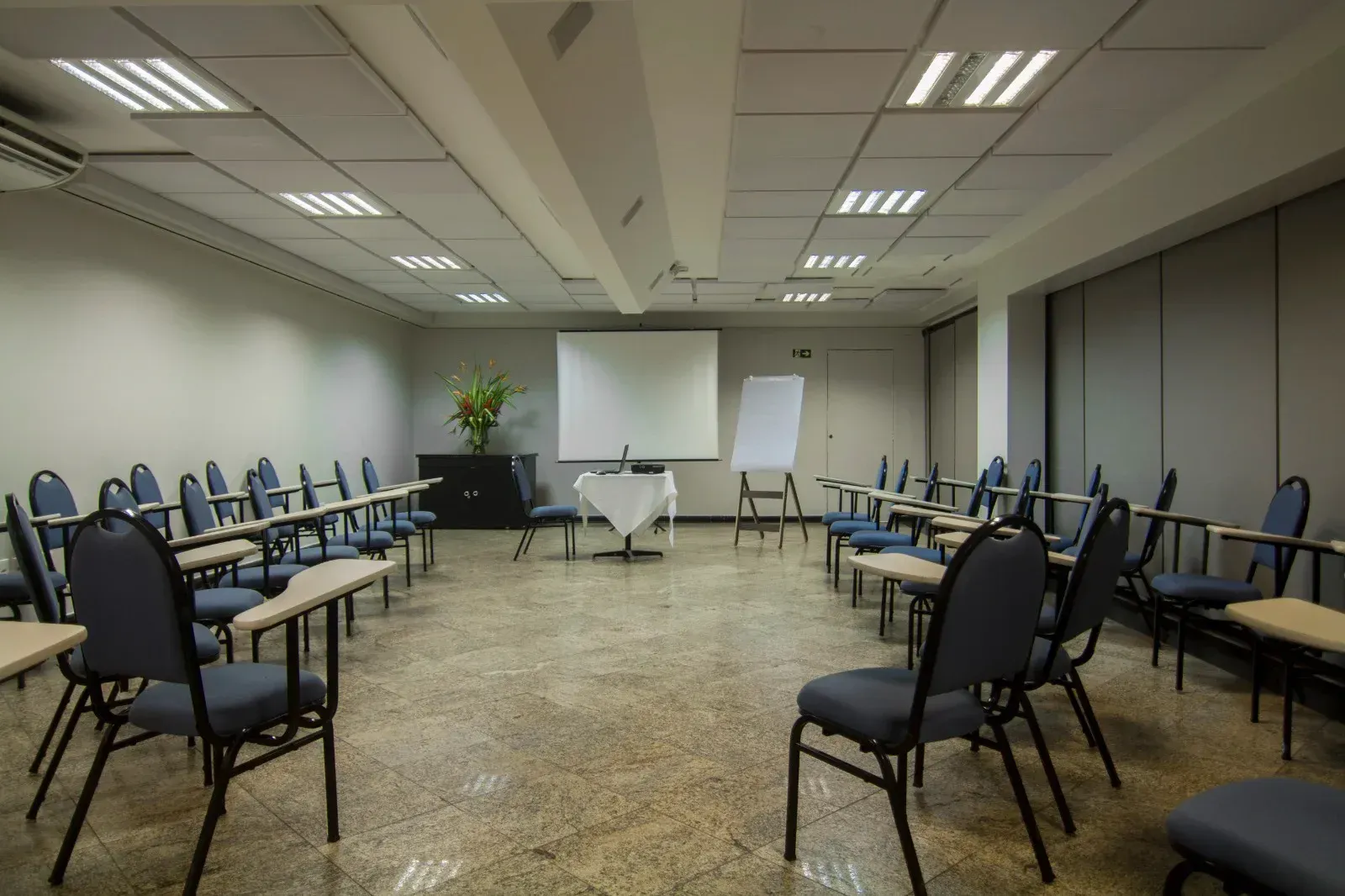 Uma sala de conferências com mesas e cadeiras e uma tela de projetor.