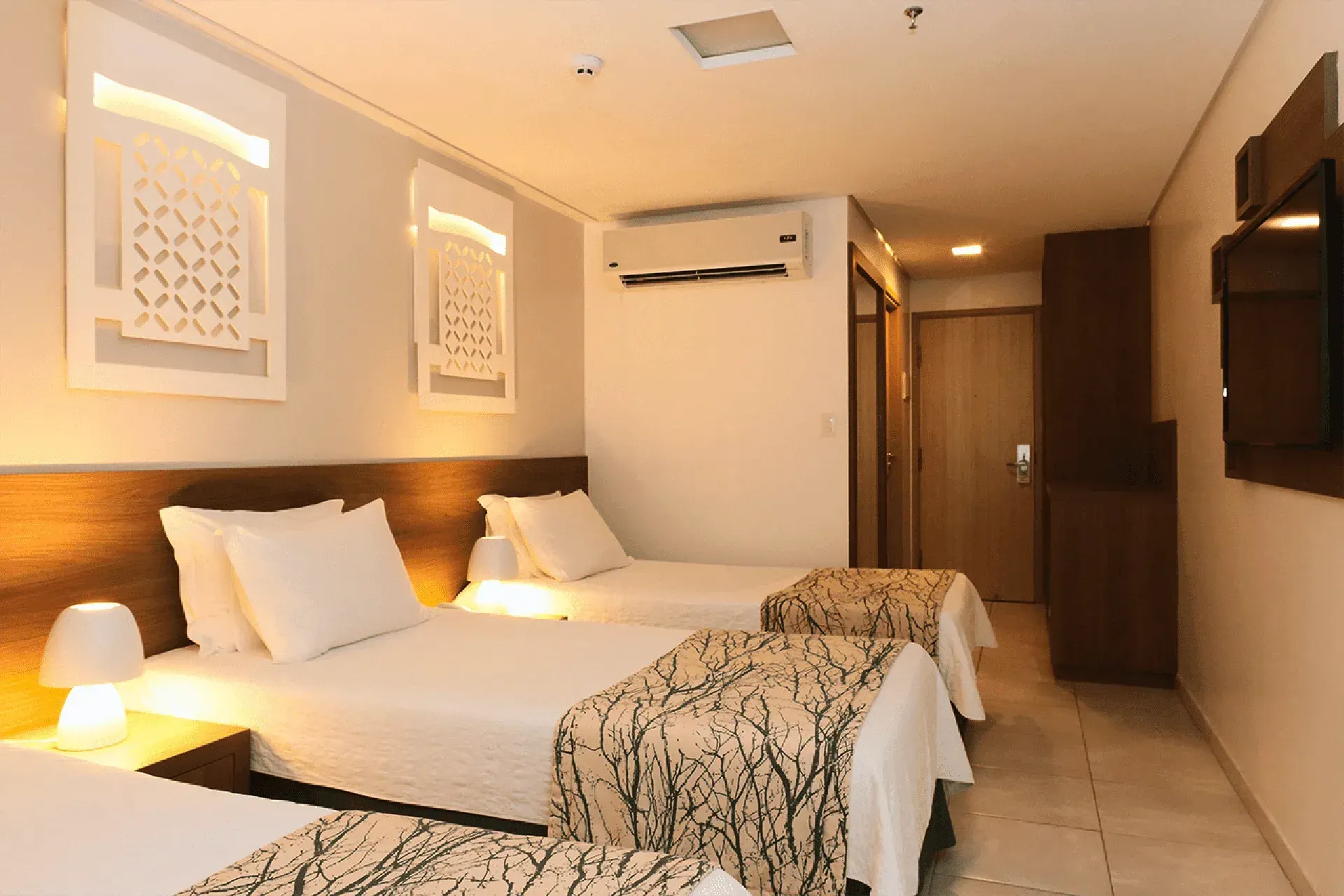 Um quarto de hotel com três camas e uma TV de tela plana.