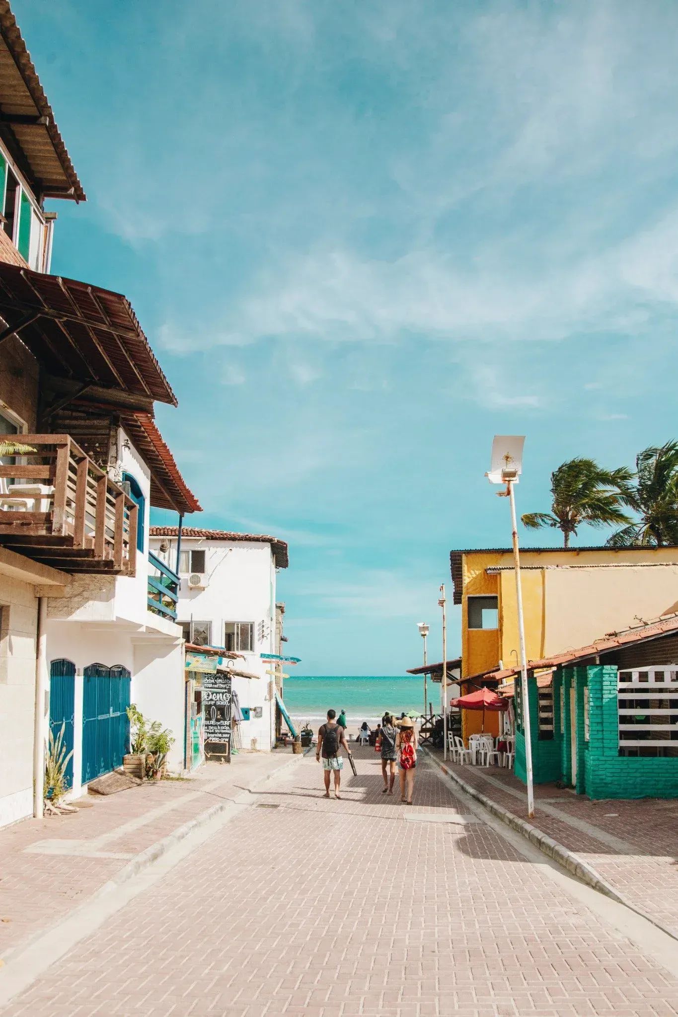 Um grupo de pessoas está caminhando por uma rua de paralelepípedos ao lado do oceano.