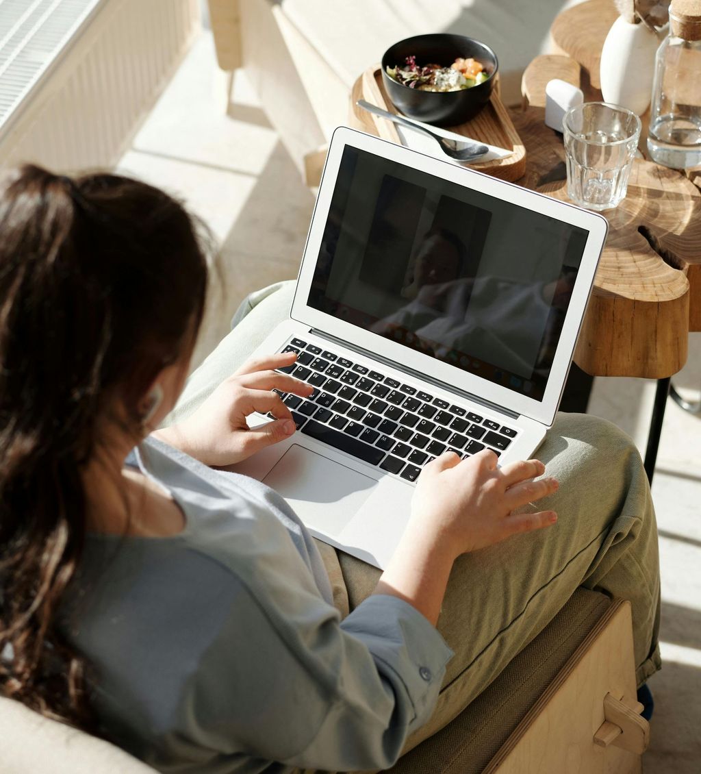 a person on her laptop on a teleconference video session. she has breakfast on the table. 