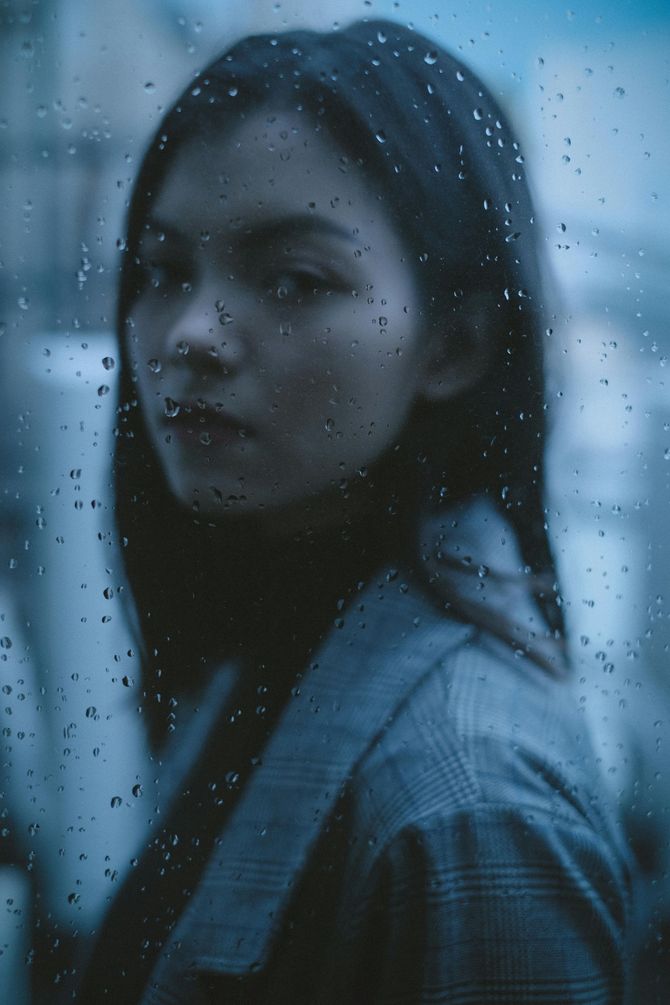 a women behind a rainy window . she has a serious expression