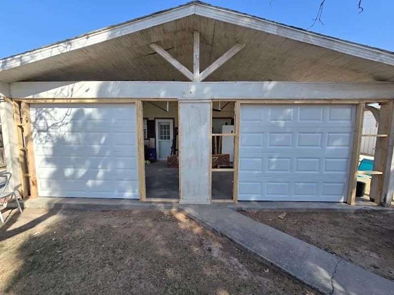 Two-car garage with white doors and concrete support beams. A walkway leads to the open interior.