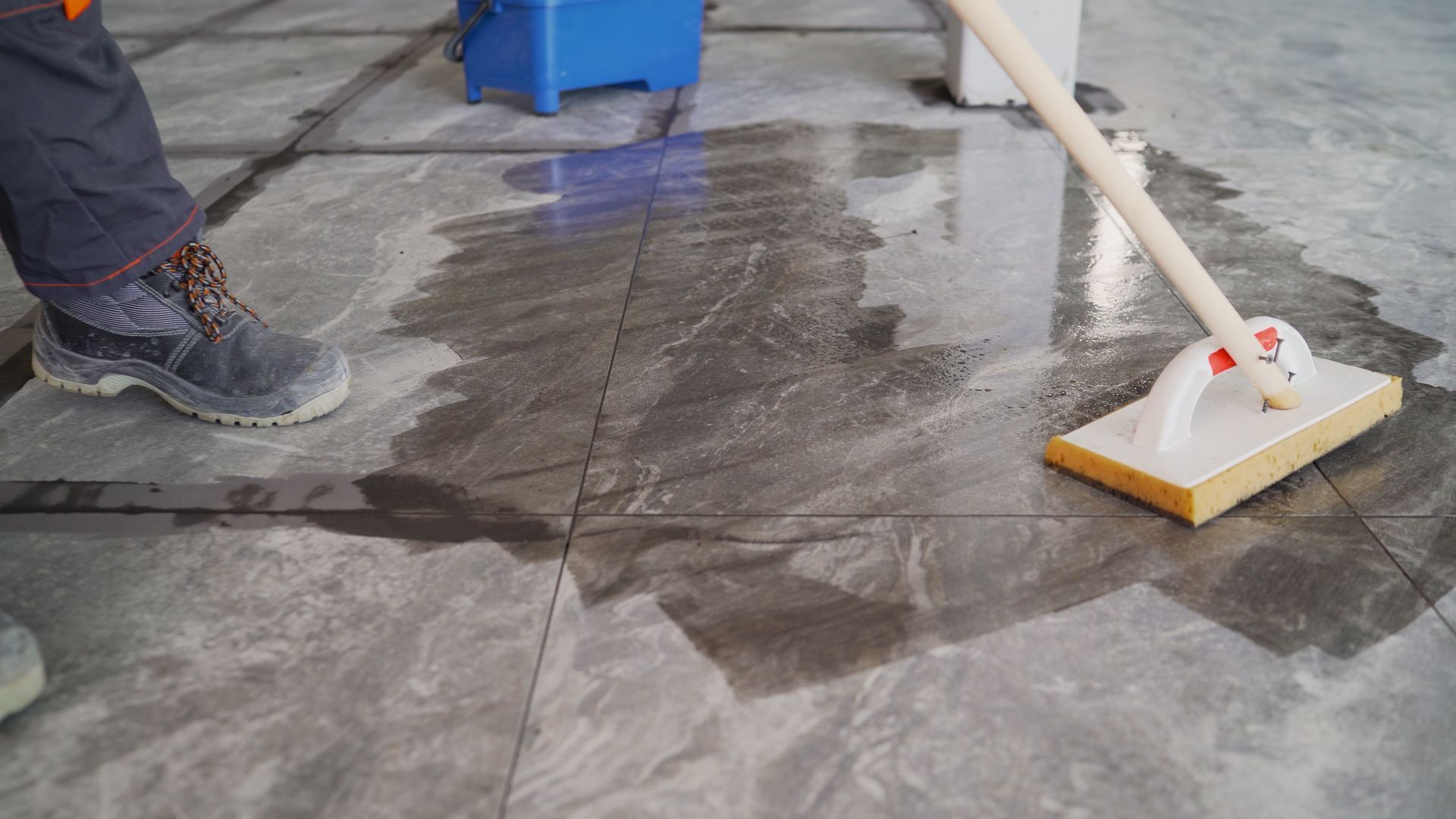 Une personne nettoie un sol carrelé avec une serpillère.