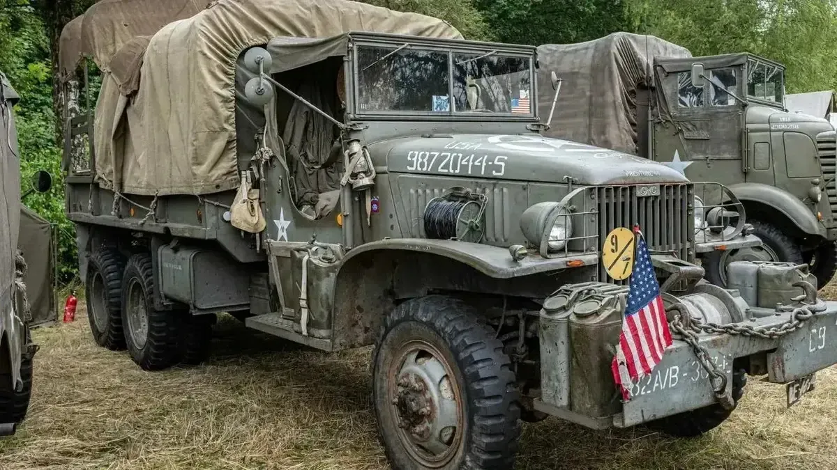 Military truck, olive green, American flag, parked outdoors. Covered cargo bed.