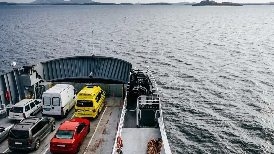 Auto transport carrier loading luxury SUVs at the port terminal with shipping cranes in the background for mainland delivery