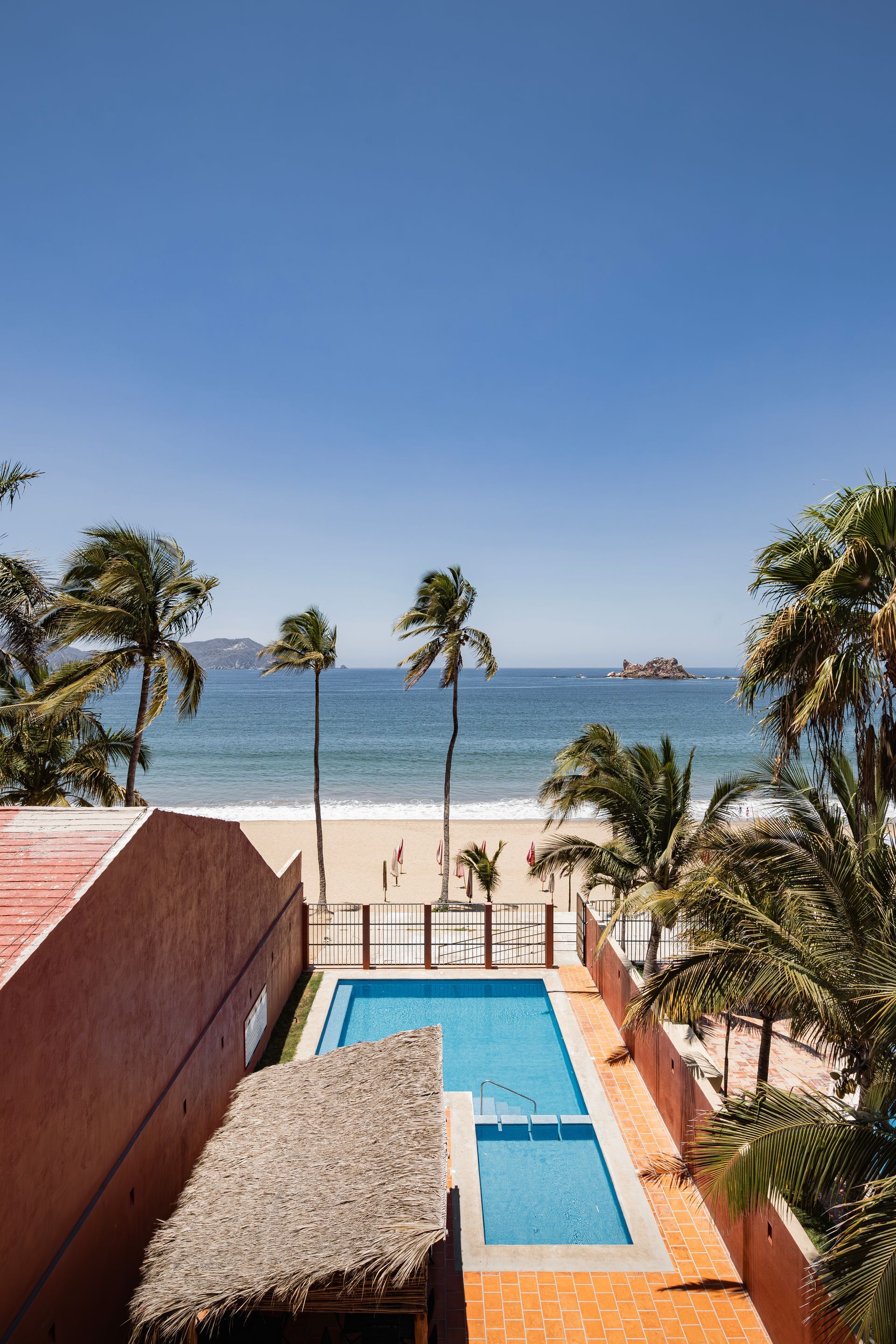 A large swimming pool surrounded by palm trees next to a beach.