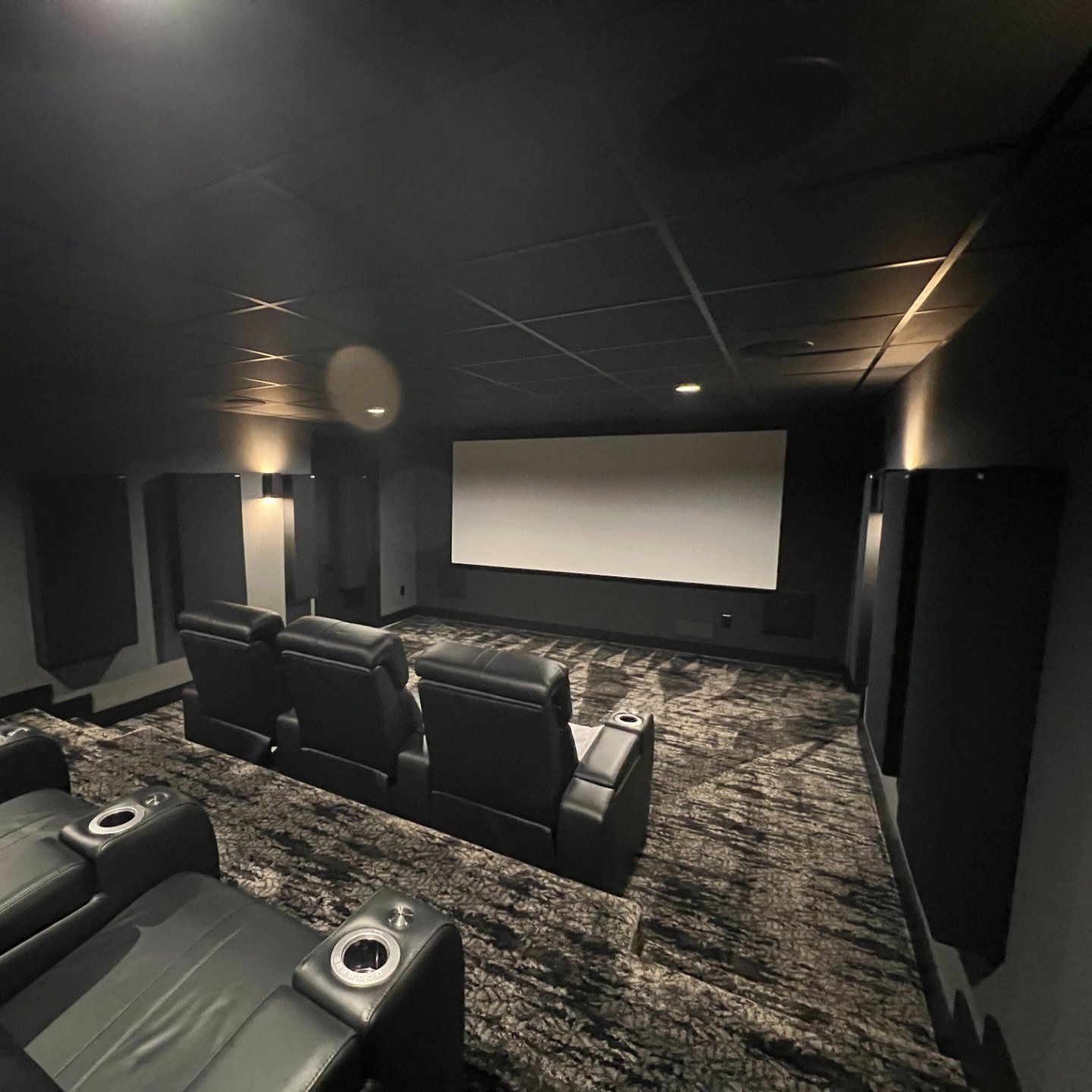 Home theater with black seats, screen, and carpet. Dark room with acoustic panels on walls.