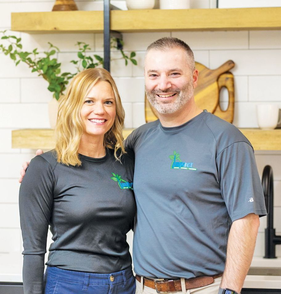 Couple in matching gray shirts with a green logo, smiling in a kitchen.