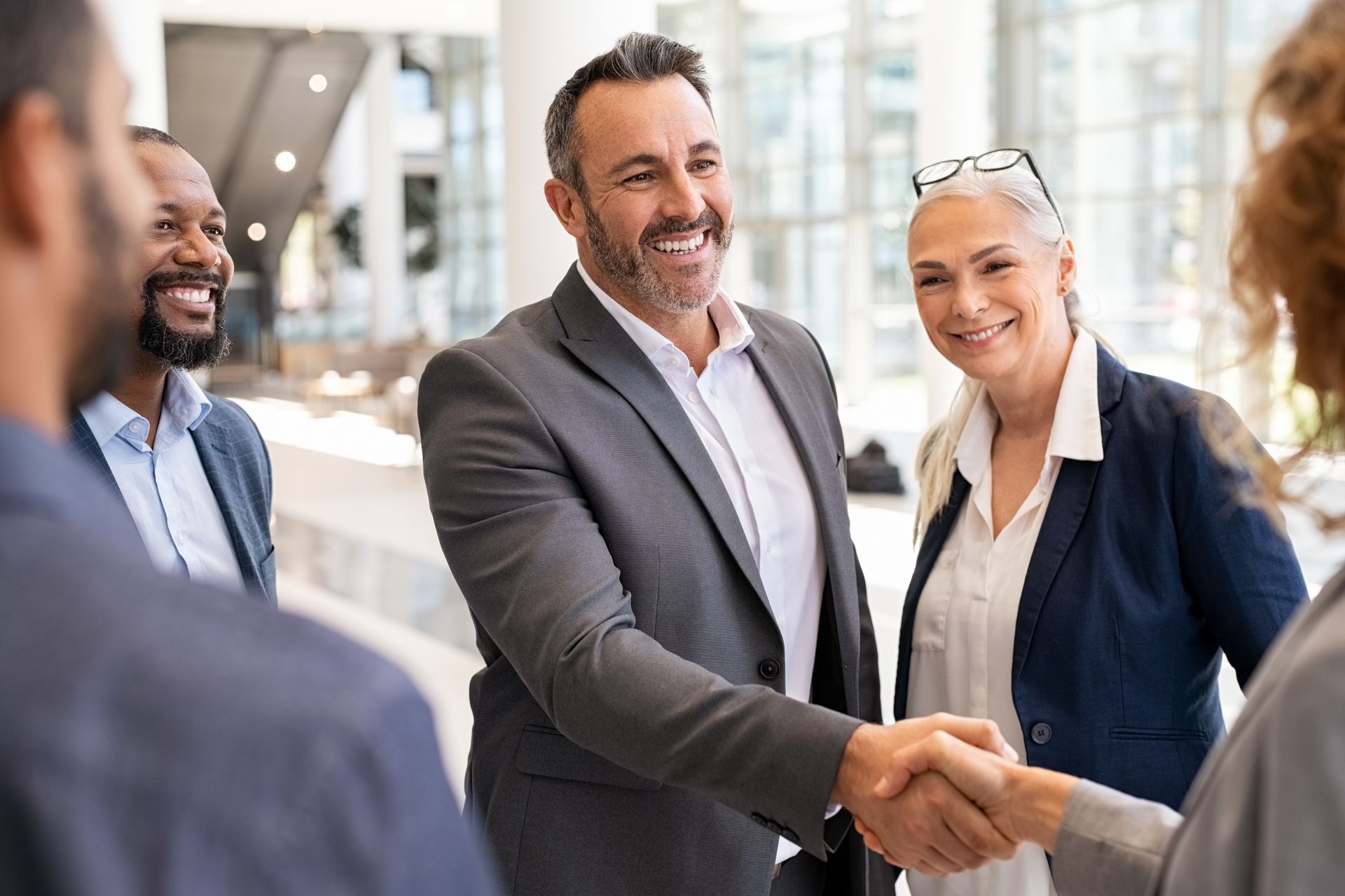 Businesspeople shaking hands, smiling, in a well-lit office setting.