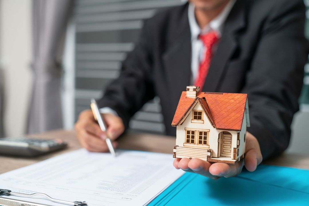 A man in a suit and tie is holding a model house in his hand.