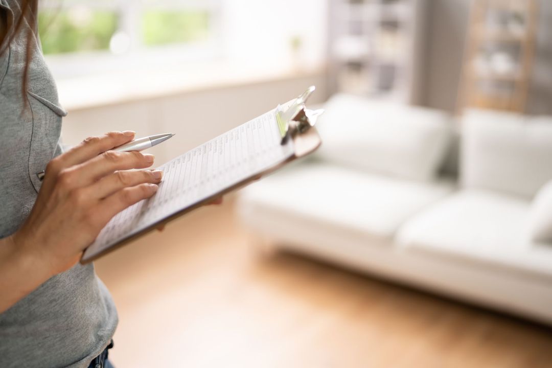 A woman is holding a clipboard and a pen in a living room.