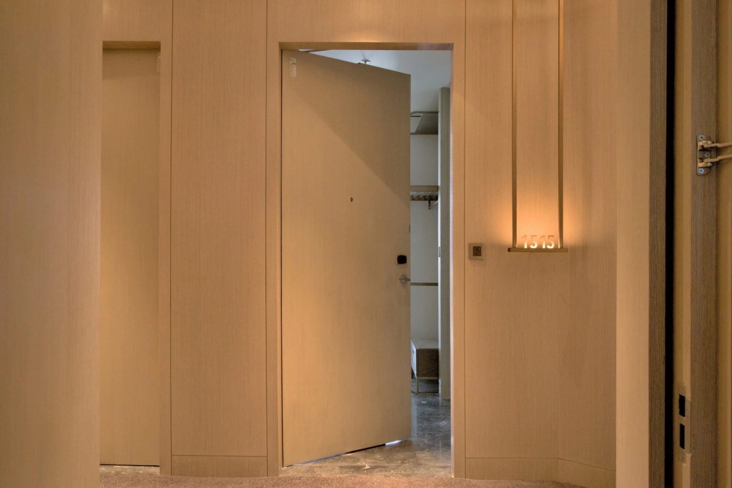 A hallway with a door that is open and a light on the wall.