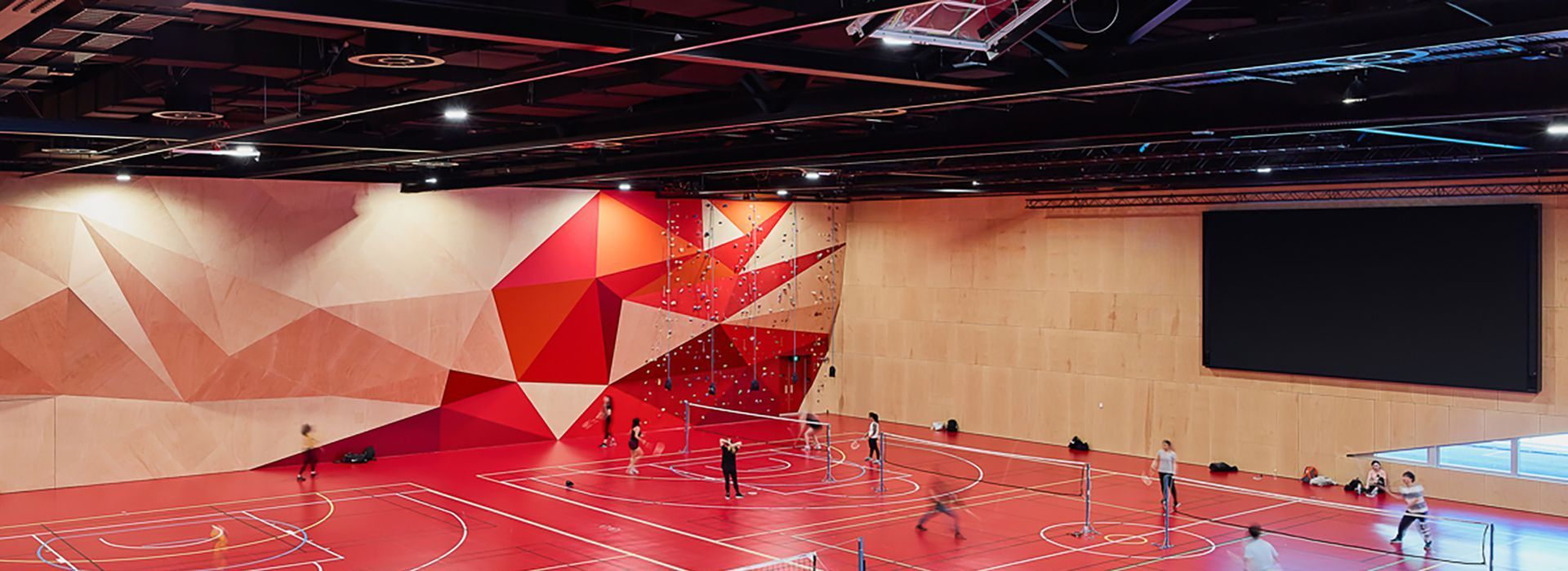 Red gym with geometric patterned wall, large screen, and people on the floor.