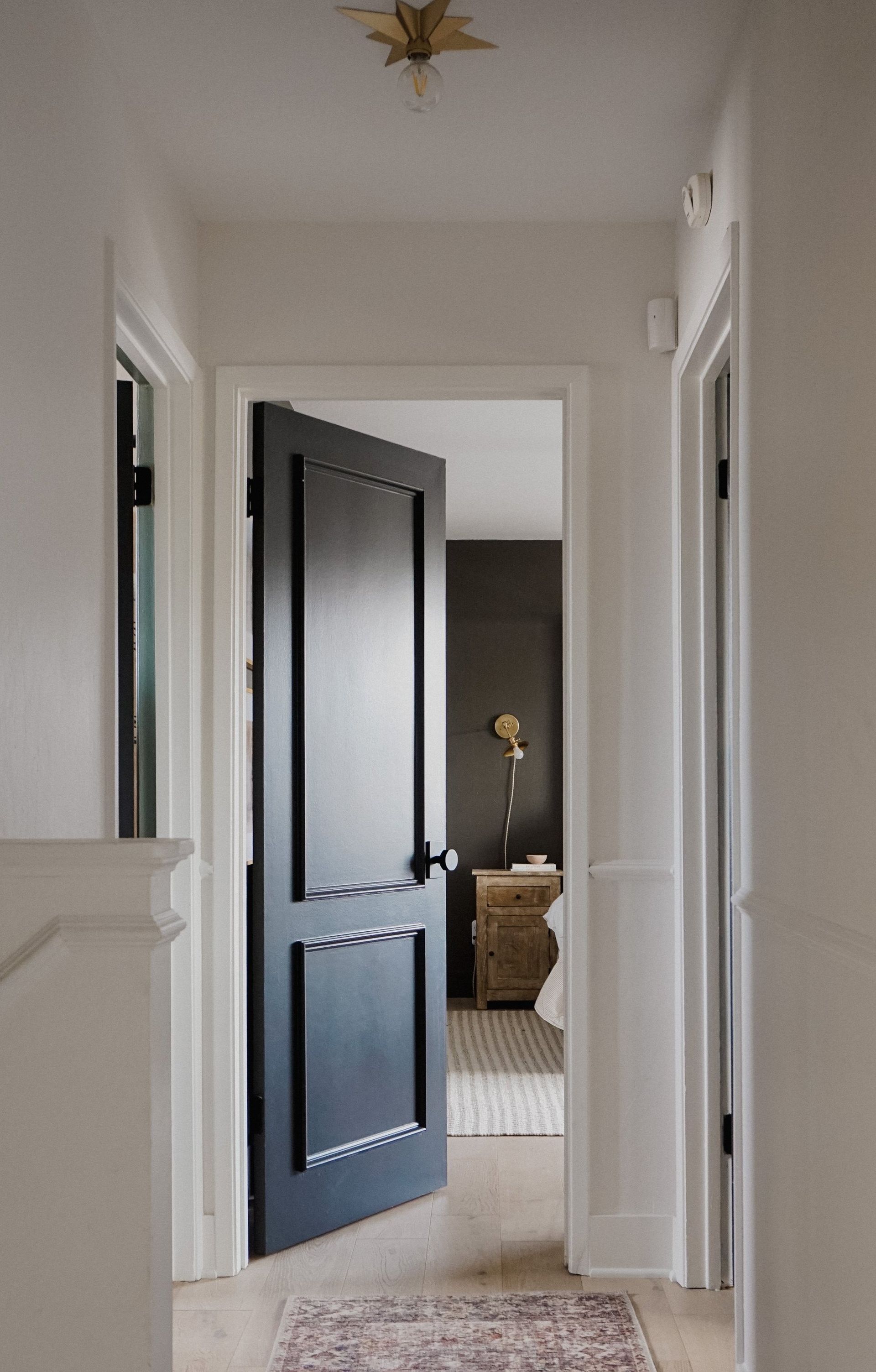 A hallway with a black door leading to a bedroom.