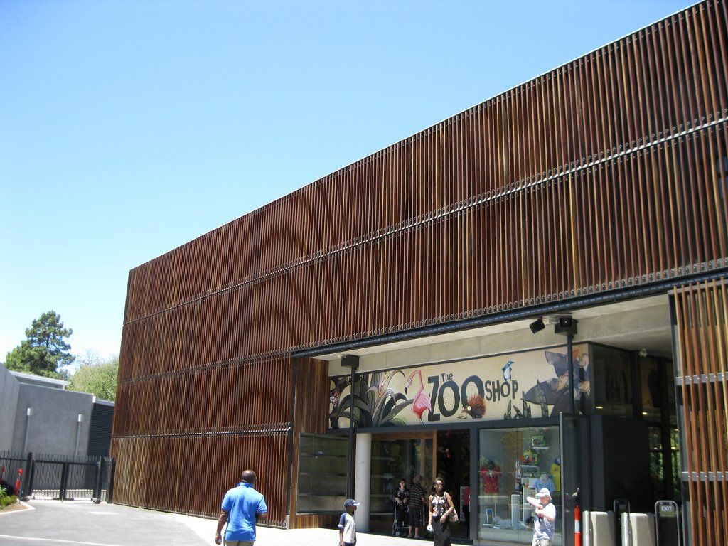 Building entrance with a brown slatted facade; people enter and exit.