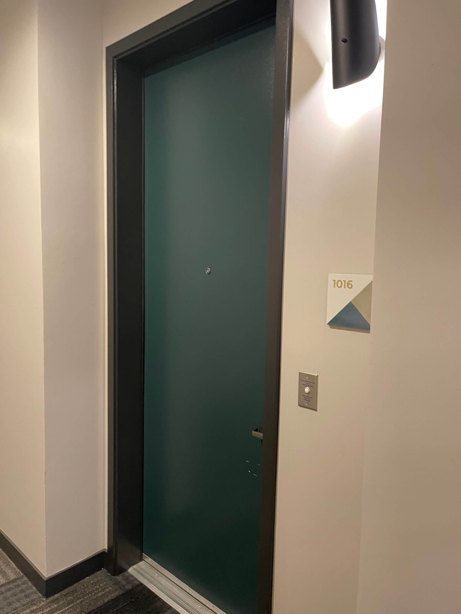 A green door is sitting in a hallway next to a wall.