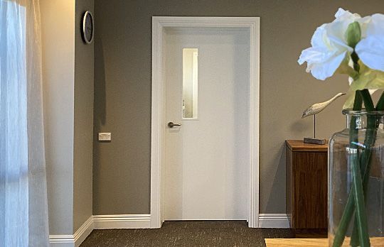 A hallway with a white door and a vase of flowers on a table.