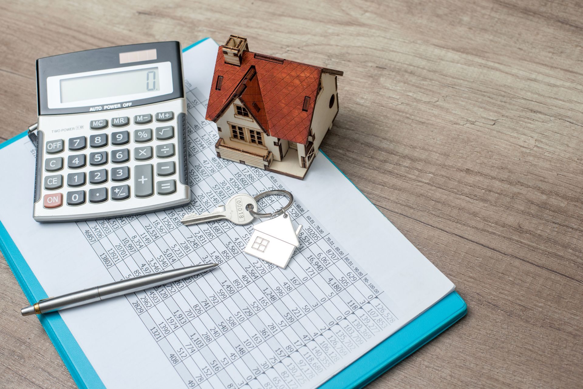 Calculator, house model, and key on financial spreadsheet for home mortgage loan planning.