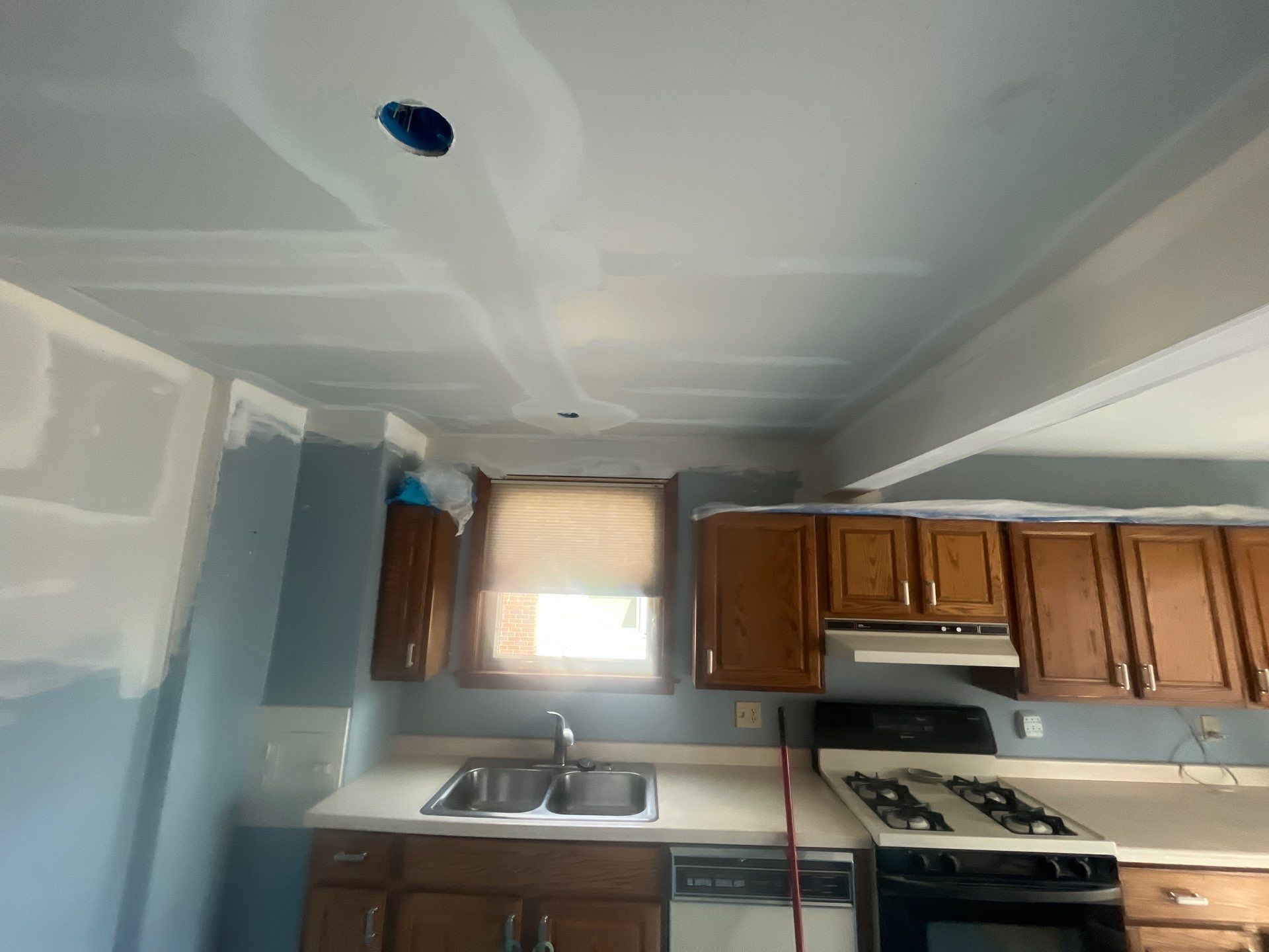 A kitchen with wooden cabinets , a stove , a sink , and a window.