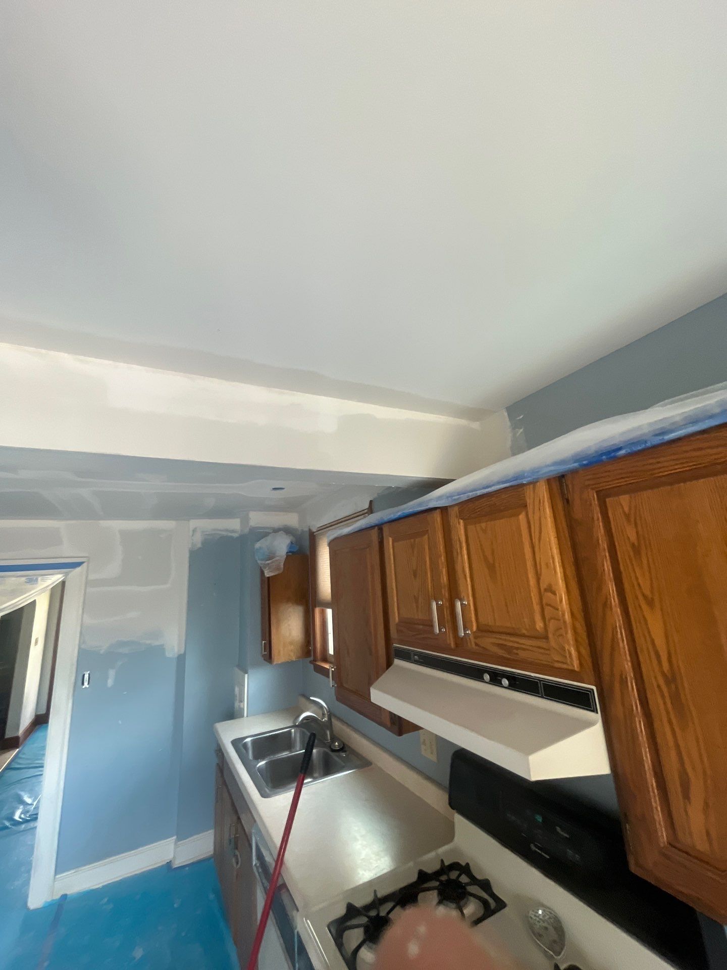 A kitchen with wooden cabinets and a stove top oven is being painted.