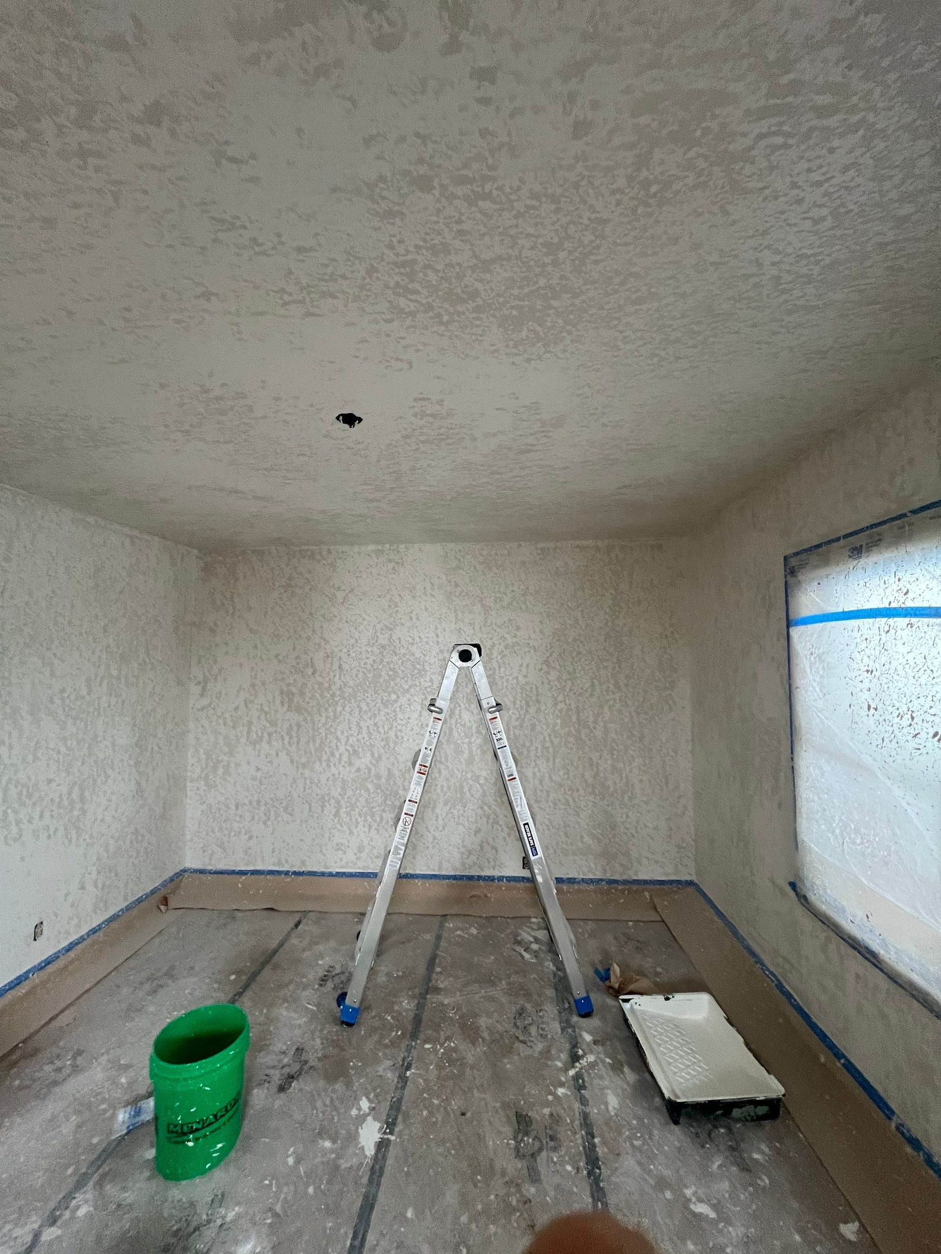 A room with a ladder and a green bucket in it.