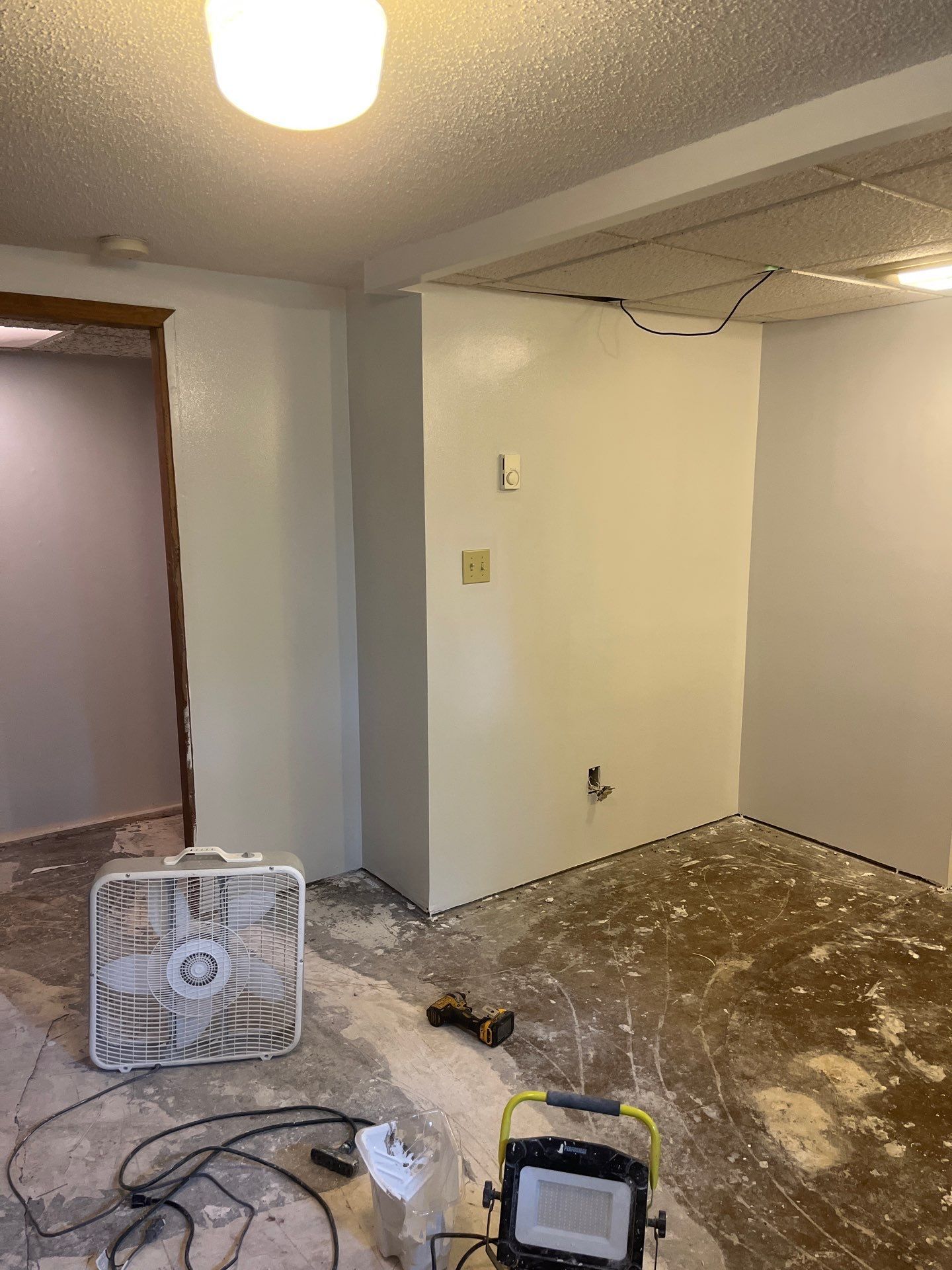 A room with white walls and a fan on the floor.