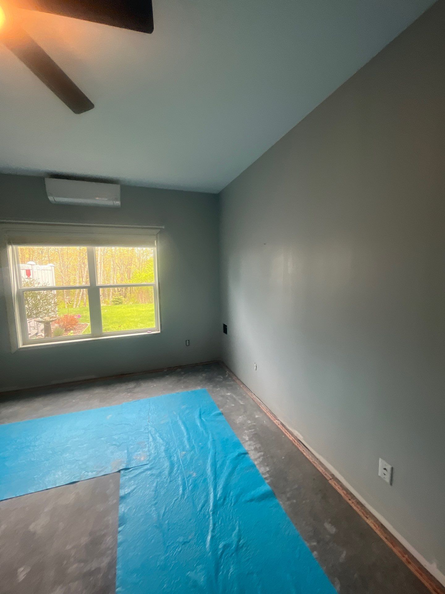 An empty room with a blue mat on the floor and a ceiling fan.