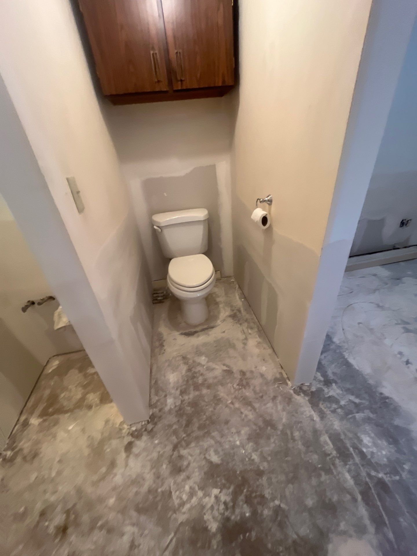 A toilet is sitting in a small bathroom with a concrete floor.