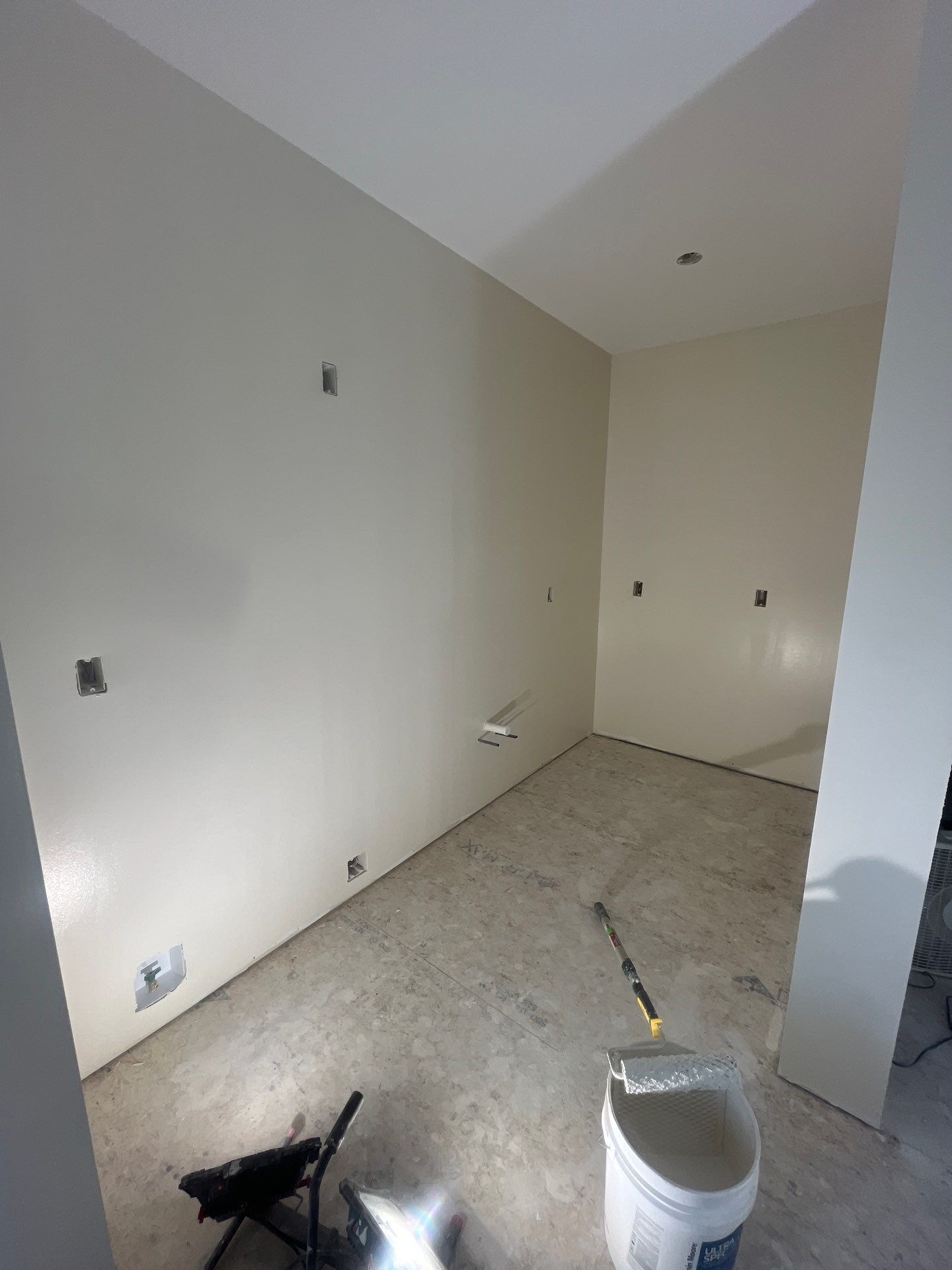 A room with white walls and a bucket of paint on the floor.