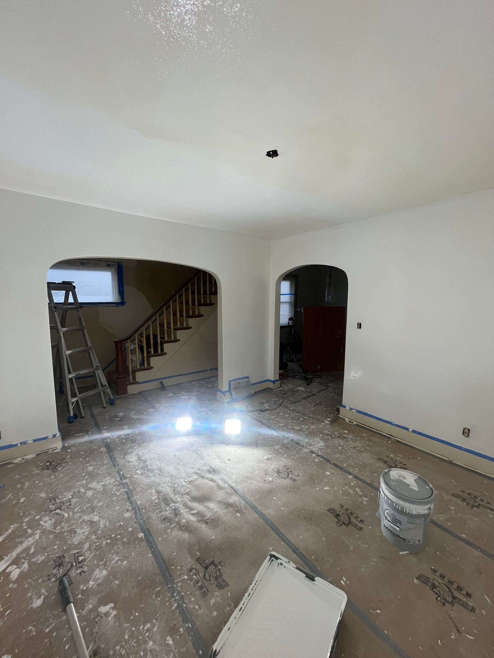 A living room with white walls and a ladder in it is being painted.