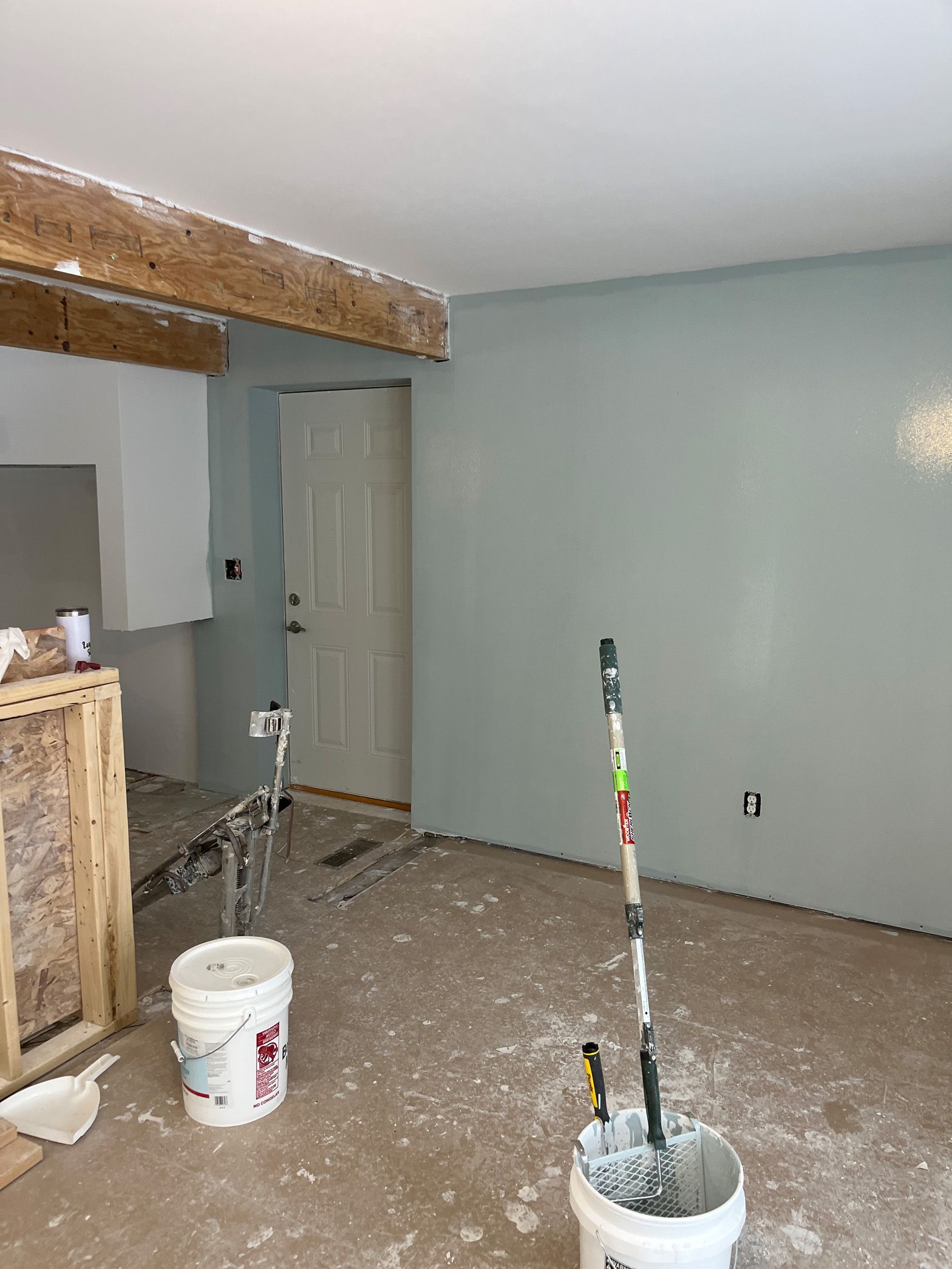 A room with a bucket of paint and a mop in it.