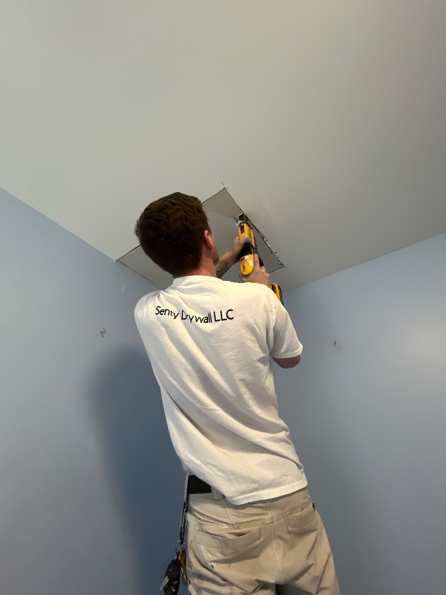 A man is using a drill to fix a hole in the ceiling.