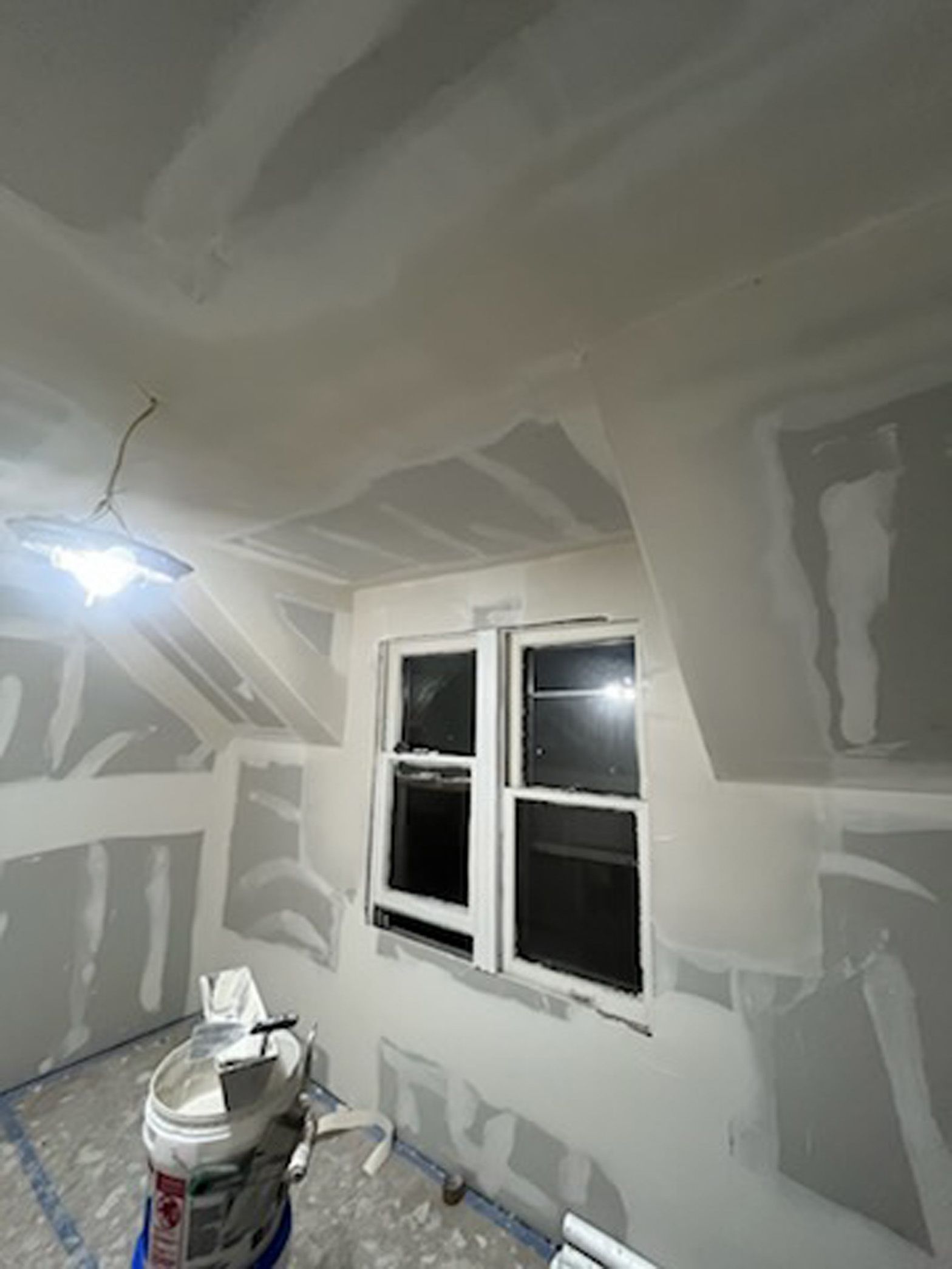 A room with a ceiling fan and two windows is being painted.